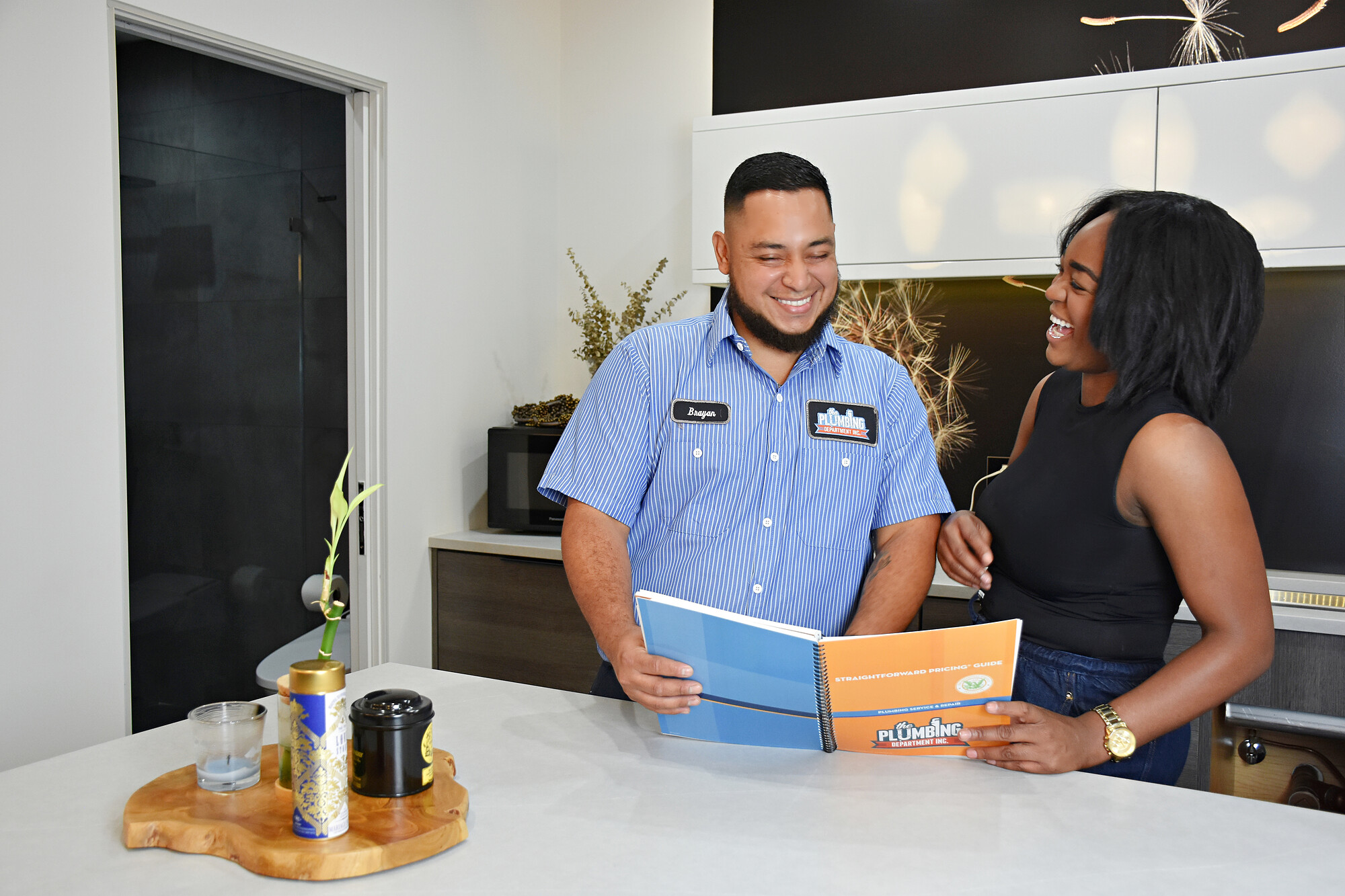 A Plumbing Department plumber going through a pricing guide with a homeowner in her kitchen.