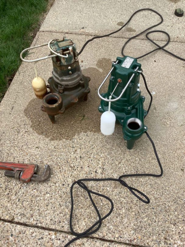 A used ejector pump sitting on the ground next to a new one.