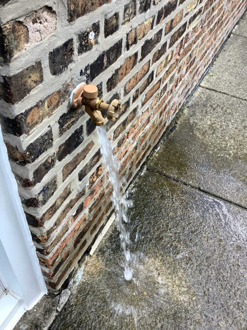 Exterior wall with running water coming out of a hose bib.