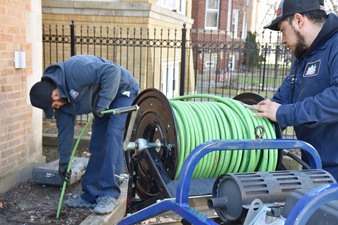 Two plumbers using a hydrojetting machine outside.